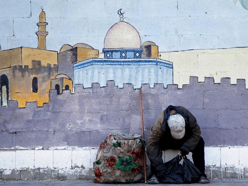 An impoverished Palestinian boy sits in front of a mural depicting the Dome of the Rock mosque in Jerusalem as he checks a bag containing things he collected from the streets in Gaza City on July 4, 2019.  MOHAMMED ABED / AFP