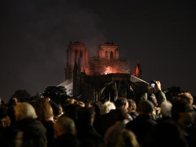 People watch as Notre-Dame de Paris Cathedral burns late into the night on April 15, 2019, in the French capital Paris.  A huge fire swept through the roof of the famed Notre-Dame Cathedral in central Paris on April 15, 2019. ludovic MARIN / AFP
