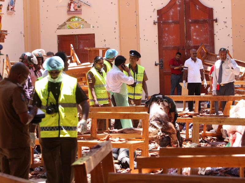 Sri Lankan security personnel walk past debris next to a dead body slumped over a bench following an explosion in St Sebastian's Church in Negombo, north of the capital Colombo, on April 21, 2019. STR / AFP