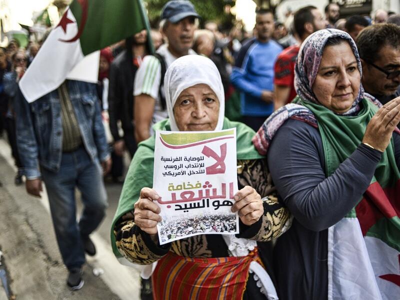 An elderly Algerian protester holds up a sign reading in Arabic "no to French guardianship, to Russian mandate, to US intervention; its excellency, the People, is master" as she marches with others draped in the national flag march during the 36th consecutive Friday anti-government demonstrations in the capital Algiers, on October 25, 2019. (RYAD KRAMDI / AFP)