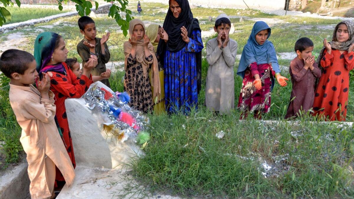 In this photograph taken on April 22, 2019, Afghan woman Niaz Bibi (C in blue), 70, and her orphaned grandchildren pray on the tombs of her sons and grandsons killed by ISIS militants in the Kot district of the Nangarhar province. NOORULLAH SHIRZADA / AFP