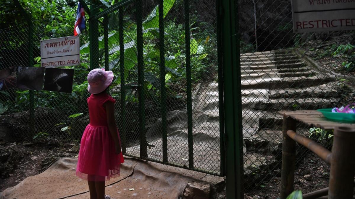 This picture taken on June 13, 2019 shows a girl looking through a gate at the entrance of the Tham Luang cave, in which 12 boys from the "Wild Boars" football team and their coach were trapped last year, in the Mae Sai district of Chiang Rai province. Lillian SUWANRUMPHA / AFP