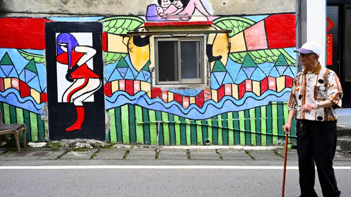 This picture taken on March 30, 2019 shows a local resident walking past a wall painted by Hakka graffiti artist Wu Tsun-hsien in the Taiwanese village of Ruan Chiao. Nestled in the mist-covered foothills of Taiwan's central mountain range, Ruan Chiao village is virtually devoid of young people, but artist Wu Tsun-hsien is coaxing the Instagram generation back by transforming local homes into a canvas of colour. Sam YEH / AFP