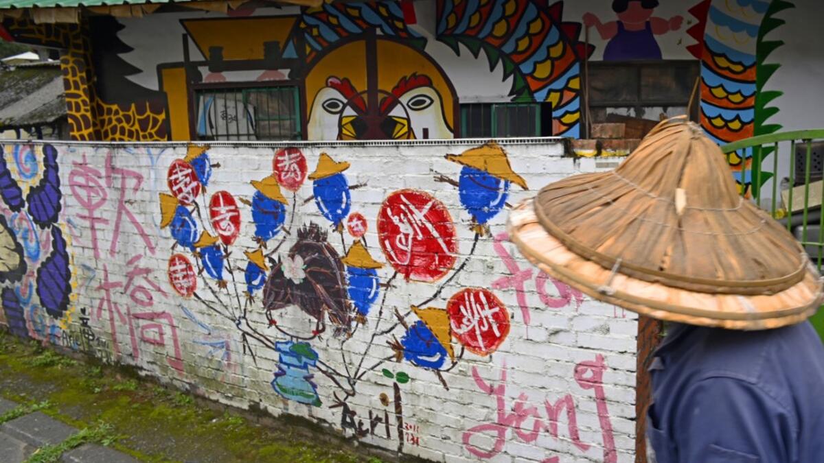 This picture taken on March 30, 2019 shows a local resident walking past a house painted by Hakka graffiti artist Wu Tsun-hsien in the Taiwanese village of Ruan Chiao. Nestled in the mist-covered foothills of Taiwan's central mountain range, Ruan Chiao village is virtually devoid of young people, but artist Wu Tsun-hsien is coaxing the Instagram generation back by transforming local homes into a canvas of colour. Sam YEH / AFP