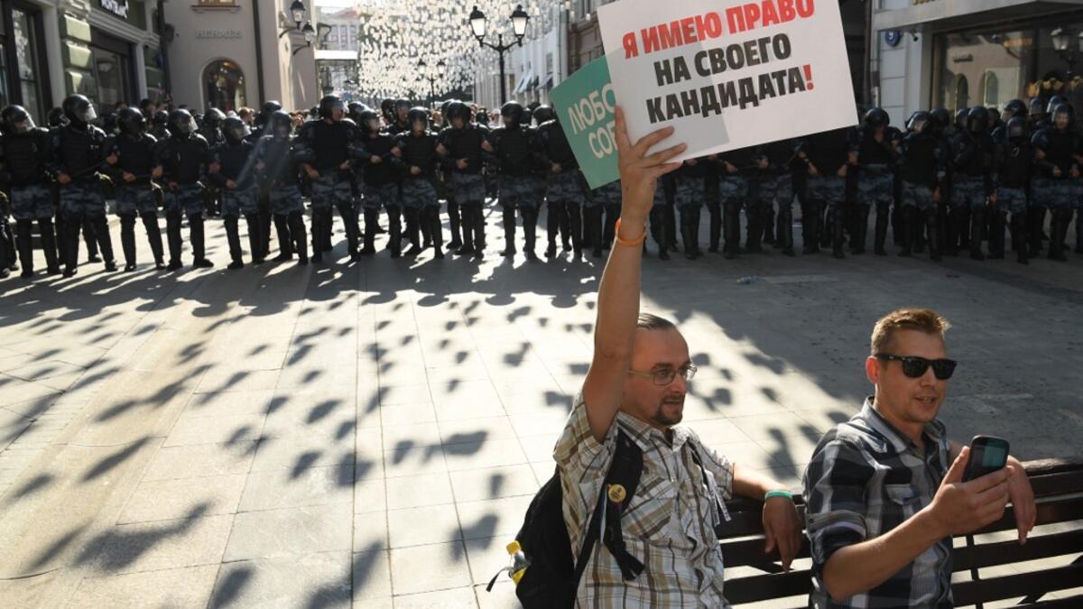A protester holding a placard reading "I have the right on my candidate" sits on a bench in front of a line of riot police during an unauthorised rally demanding independent and opposition candidates be allowed to run for office in local election in September, in downtown Moscow on July 27, 2019.  Kirill KUDRYAVTSEV / AFP
