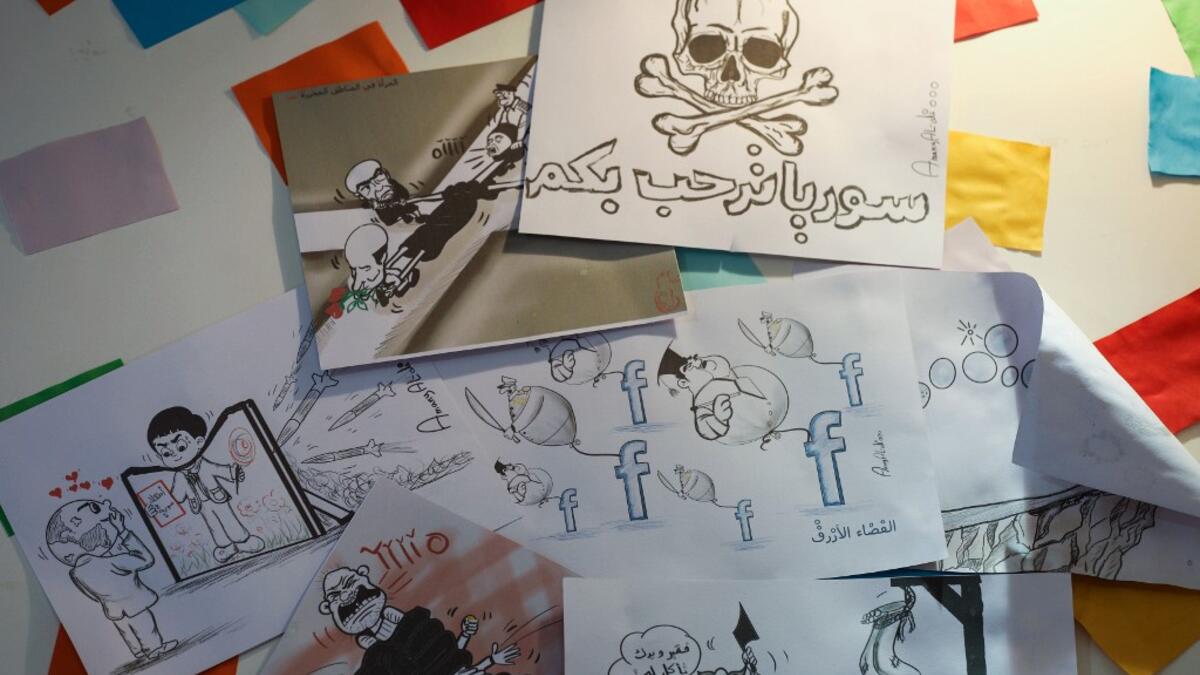 This picture shows illustrations by Syrian Cartoonist Amani al-Ali at her home studio in the city of Idlib in the eponymous northwestern province, including a drawing of a skull and crossbones with a caption below reading in Arabic "Syria welcomes you", and another of a woman being pulled from four sides by different men.  Omar HAJ KADOUR / AFP