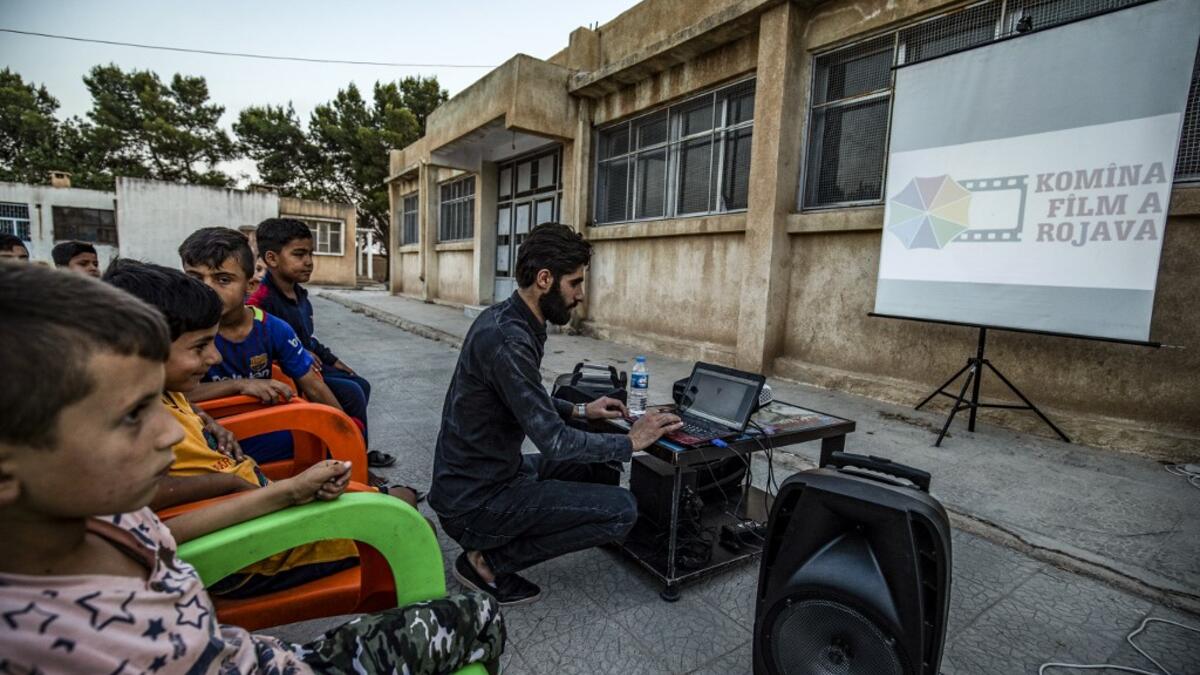 A member of Syrian-Kurdish filmmaker Shero Hinde's mobile cinema "Komina Film" initiative prepares a laptop connected to a projector and screen for a film screening for children at a school yard in the village of Shaghir Bazar, 55 kilometres southest of Qamishli in the Kurdish-populated areas of northeastern Syria's Hasakeh province, on July 28, 2019. DELIL SOULEIMAN / AFP