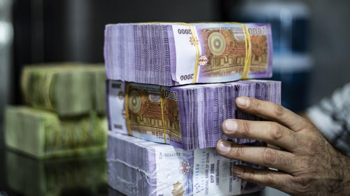 A merchant arranges stacks of Syrian pounds at a market in the Kurdish-majority city of Qamishli in northeast Syria on September 10, 2019. The declining value of the pound is a sure sign of Syria's ailing economy. The civil war has battered the country's finances and depleted its foreign reserves. A flurry of international sanctions on President Bashar al-Assad's regime and associated businessmen since the start of the war in 2011 has compounded the situation.  Delil SOULEIMAN / AFP