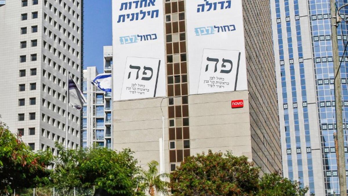 An Ultra-Orthodox Jewish man walks along a street in the Israeli coastal city of Tel Aviv on September 12, 2019, as electoral billboards are seen in the background off the facade of a building showing the faces of (L to R) Yair Lapid and retired general Benny Gantz, two of the leaders of the "Blue and White" (Kahol Lavan) electoral alliance vying for seats in the upcoming September 17 vote. Gil COHEN-MAGEN / AFP