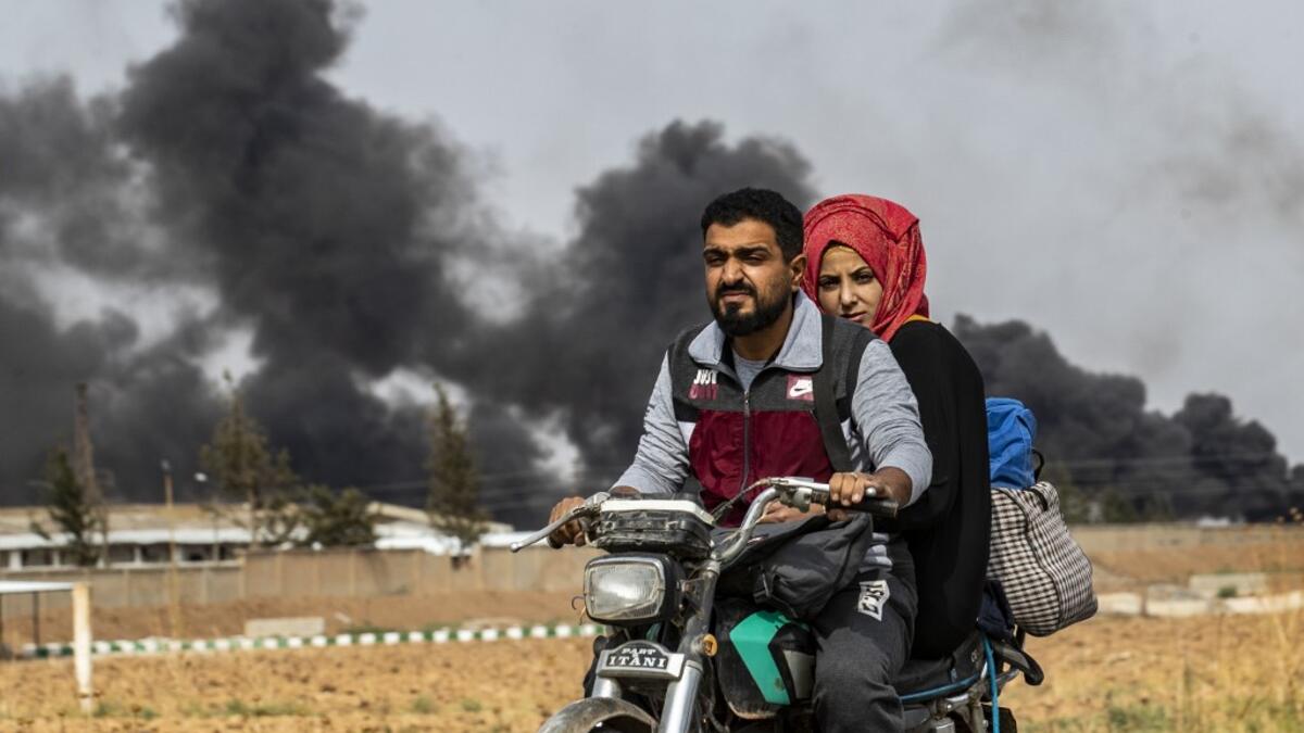 A Syrian couple use a motorcycle to flee the countryside of the northeastern Syrian town of Ras al-Ain on the Turkish border, toward the west to the town of Tal Tamr on October 19, 2019. The smoke behind them is from burning tyres used to impede visibility from warplanes. Delil SOULEIMAN / AFP