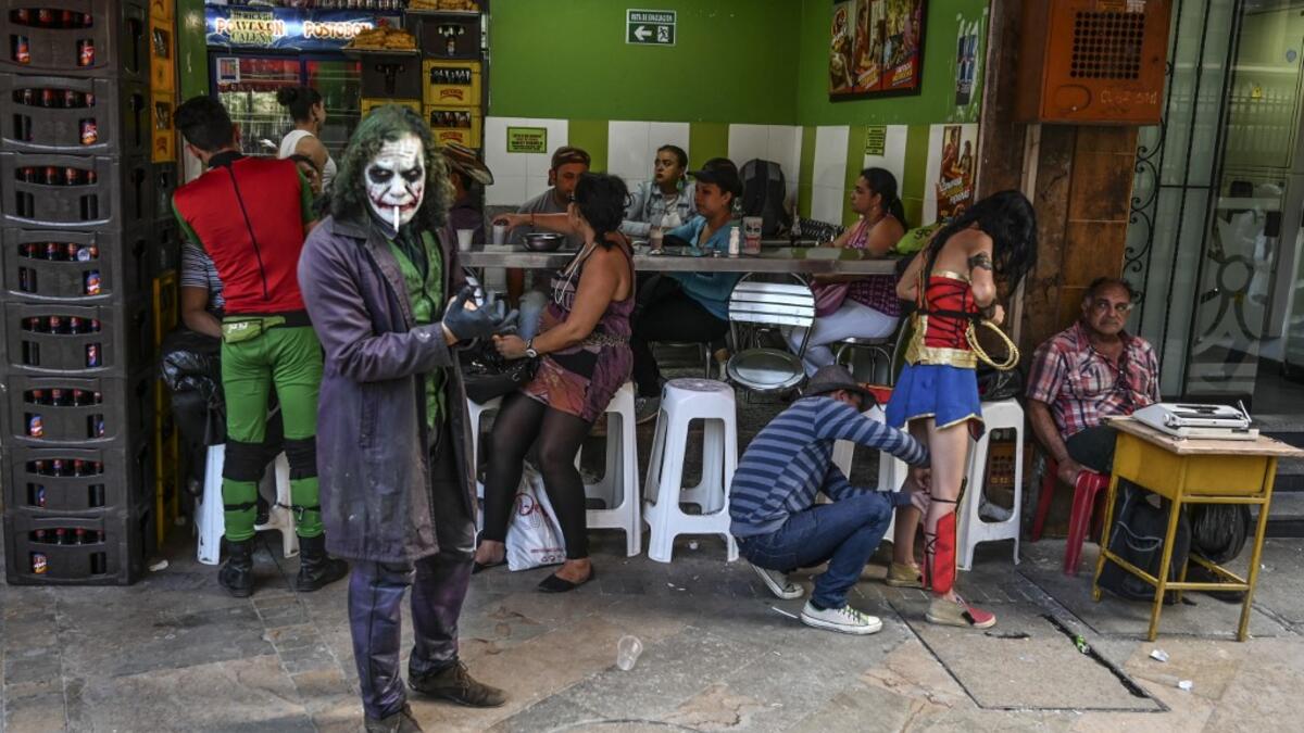 Venezuelan migrant Johnny Tales (L), who makes a living imitating the comicbook and film character "The Joker", smokes a cigarette as fellow compatriots also fancy dressed as comic and film industry characters prepare to perform in Medellin, on October 29, 2019. JOAQUIN SARMIENTO / AFP