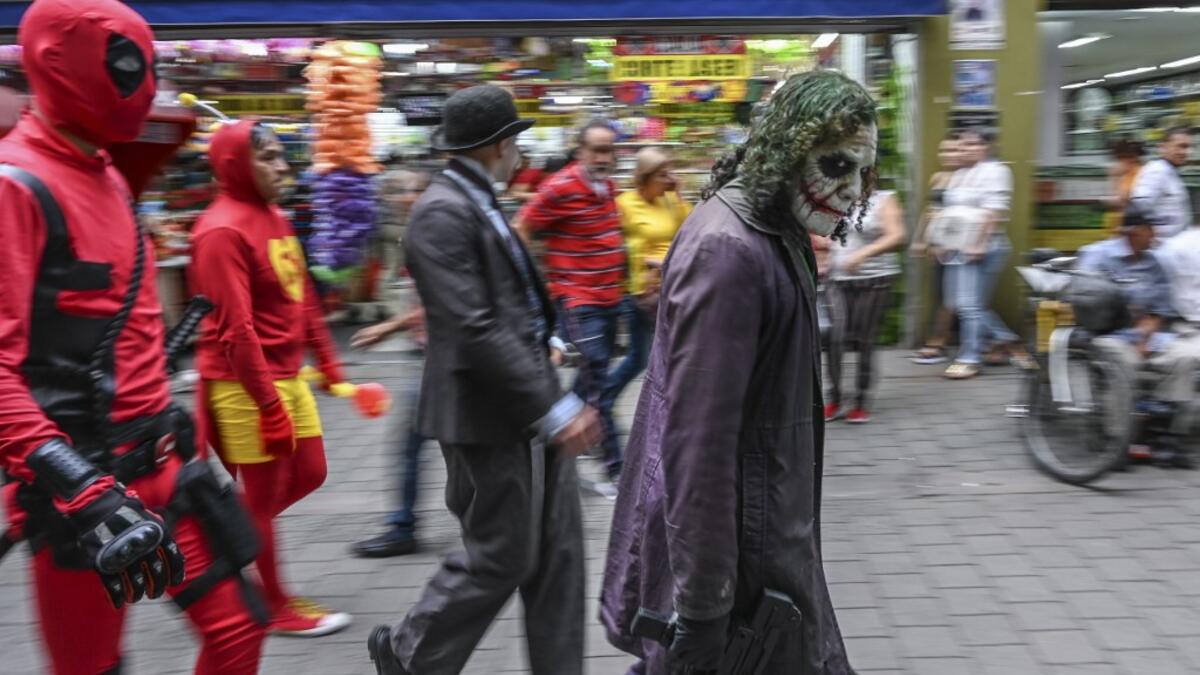 Venezuelan migrant Johnny Tales (R), who makes a living imitating the comicbook and film character "The Joker", performs followed by fellow compatriots also fancy dressed as comic and film industry characters along a street in Medellin, on October 29, 2019. JOAQUIN SARMIENTO / AFP