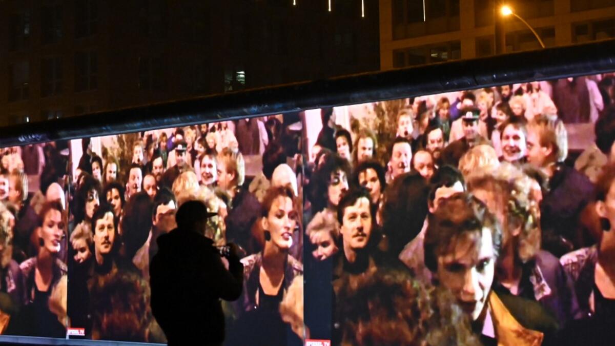 A spectators stands in front of a 3D video installation projected on the so-called East Side Gallery, a 1,3 km-long portion of the Berlin wall, during a rehearsal on November 3, 2019 in Berlin.  Tobias SCHWARZ / AFP