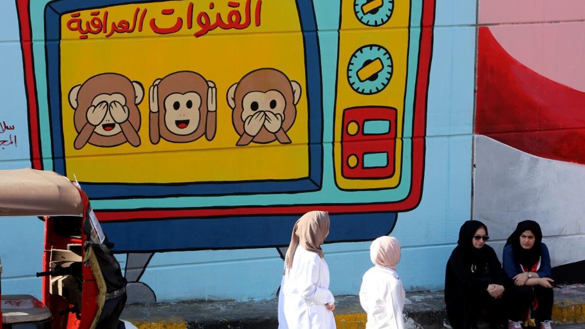 Iraqi women are pictured in front of a colourful mural in Baghdad on November 6, 2019 representing Iraqi TV channels, "that do not want to see, hear or speak about" the anti-government protests that have engulfed Iraq since early October. A mounting death toll in Baghdad and across southern Iraq coupled with renewed internet restrictions sparked fears that anti-government protests would once again trigger chaos. SABAH ARAR / AFP