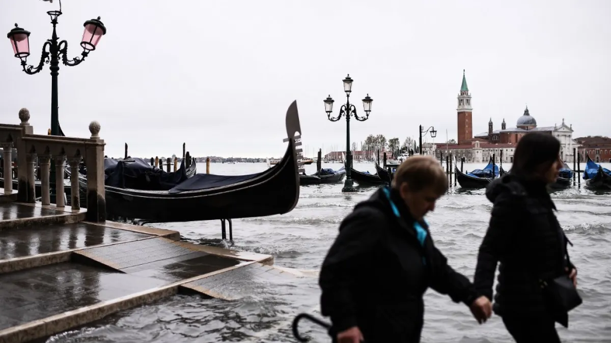 People walk across the Ponte della Paglia bridge, past a stranded gondola after an exceptional overnight "Alta Acqua" high tide water level, early on November 13, 2019 in Venice. Powerful rainstorms hit Italy on November 12, with the worst affected areas in the south and Venice, where there was widespread flooding. Within a cyclone that threatens the country, exceptional high water were rising in Venice, with the sirocco winds blowing northwards from the Adriatic sea against the lagoon’s outlets and prevent