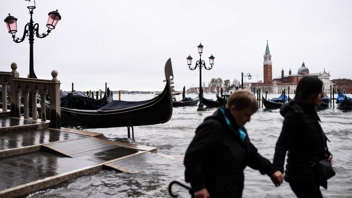 People walk across the Ponte della Paglia bridge, past a stranded gondola after an exceptional overnight "Alta Acqua" high tide water level, early on November 13, 2019 in Venice. Powerful rainstorms hit Italy on November 12, with the worst affected areas in the south and Venice, where there was widespread flooding. Within a cyclone that threatens the country, exceptional high water were rising in Venice, with the sirocco winds blowing northwards from the Adriatic sea against the lagoon’s outlets and prevent