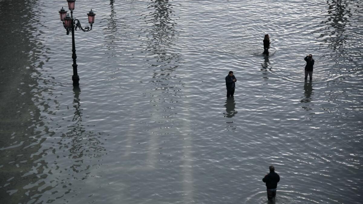 People walk across and take photos at the flooded St. Mark's Square after an exceptional overnight "Alta Acqua" high tide water level, on November 13, 2019 in Venice. Venice was hit by the highest tide in more than 50 years late November 12, with tourists wading through flooded streets to seek shelter as a fierce wind whipped up waves in St. Mark's Square. Marco Bertorello / AFP