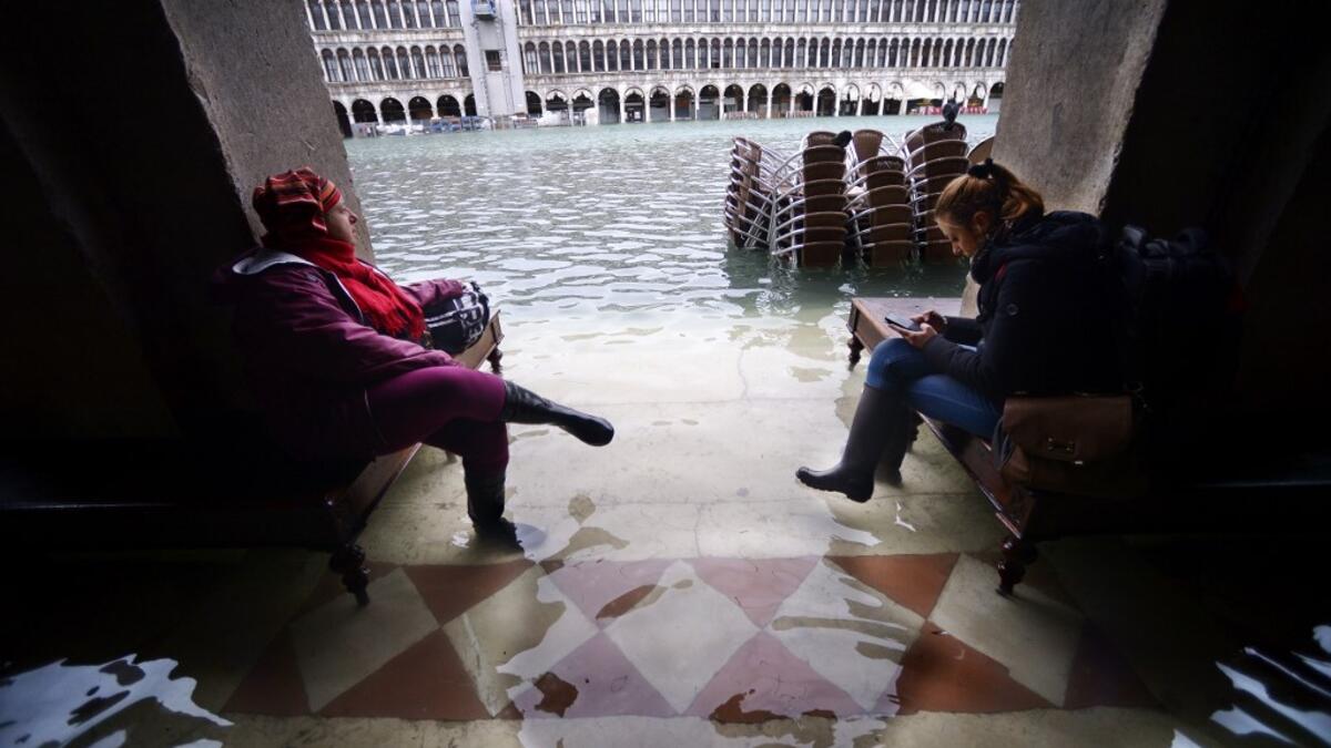 People sit on benches in a flooded arcade by St. Mark's Square on November 15, 2019 in Venice, two days after the city suffered its highest tide in 50 years. Flood-hit Venice was bracing for another exceptional high tide on November 15, as Italy declared a state of emergency for the UNESCO city where perilous deluges have caused millions of euros worth of damage. Filippo MONTEFORTE / AFP