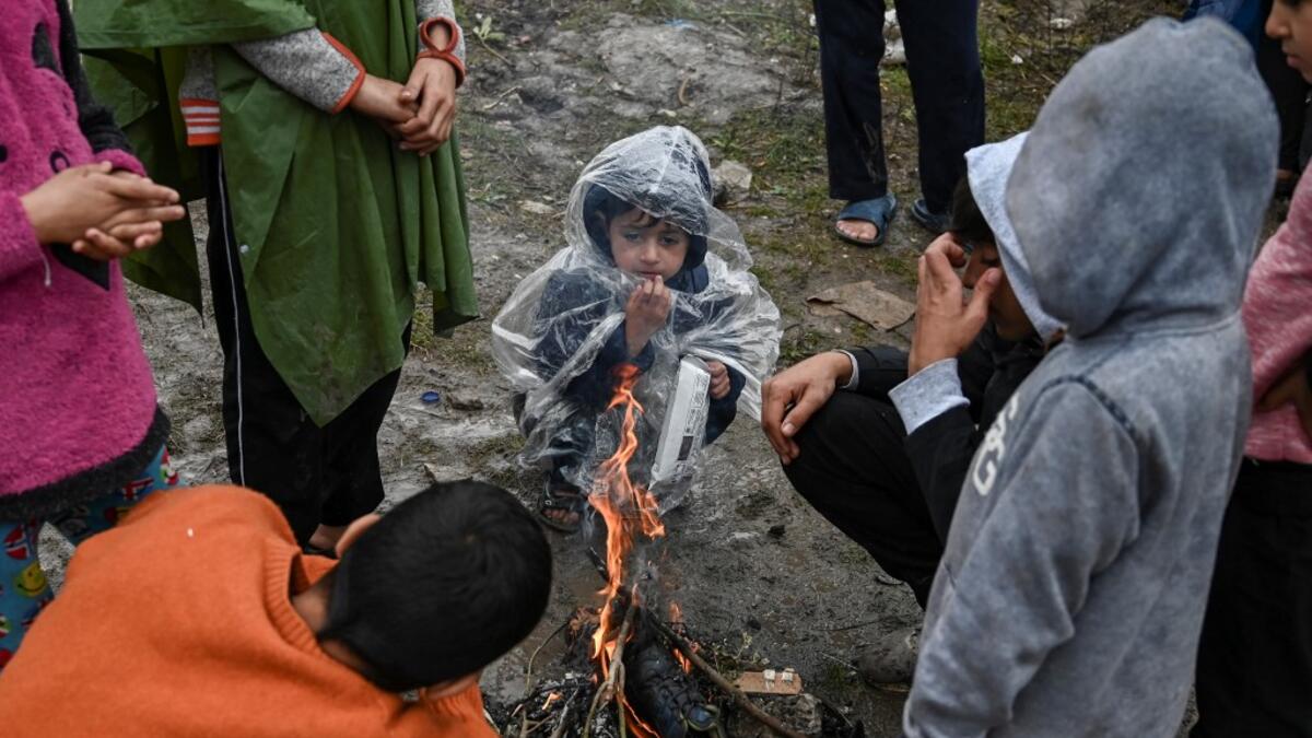 Children warm themselves around a camp fire under the rain in the refugee camp of Moria, on the island of Lesbos on November 26, 2019. Conditions remain difficult in the overcrowded Moria camp in Greece with winter fast approaching. The government announced on November 20it will shut down the three largest of its overcrowded migrant camps on islands facing Turkey, and replace them with new closed facilities with much larger capacity. ARIS MESSINIS / AFP