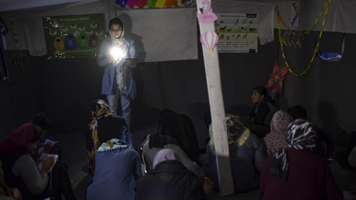 A woman gives evening English lessons to migrants and refugees with a flashlight as they don't have electricity at a makeshift camp next to the camp of Moria in the Greek island of Lesbos on November 29, 2019. ARIS MESSINIS / AFP