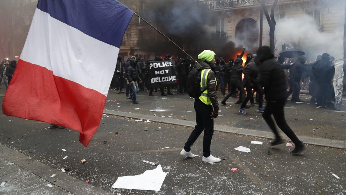 A man holding a French flag and a yellow vest walks in tear gas as protestors gesture in the background during a demonstration against the pension overhauls, in Paris, on December 5, 2019 as part of a nationwide strike. Zakaria ABDELKAFI / AFP