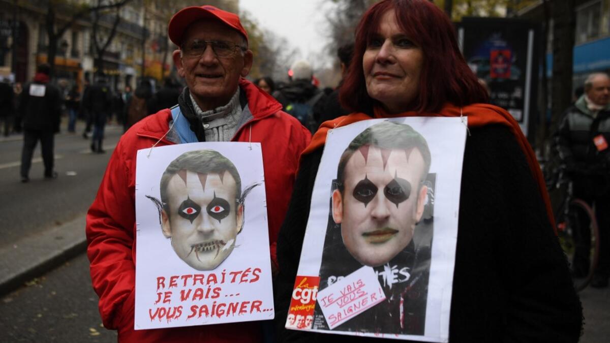 A man and a woman hold signs reading "Pensioners, I will bleed you" and bearing pictures mocking French President Emmanuel Macron during a demonstration against the pension overhauls, in Paris, on December 5, 2019 as part of a nationwide strike. ALAIN JOCARD / AFP