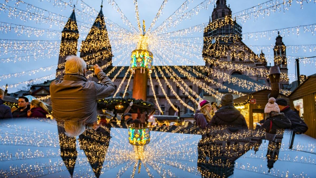 A man photographs the cathedral and the festive lighting of the Christmas market as they mirror on a polished surface in Mainz, Germany, on December 6, 2019.  Frank Rumpenhorst / dpa / AFP