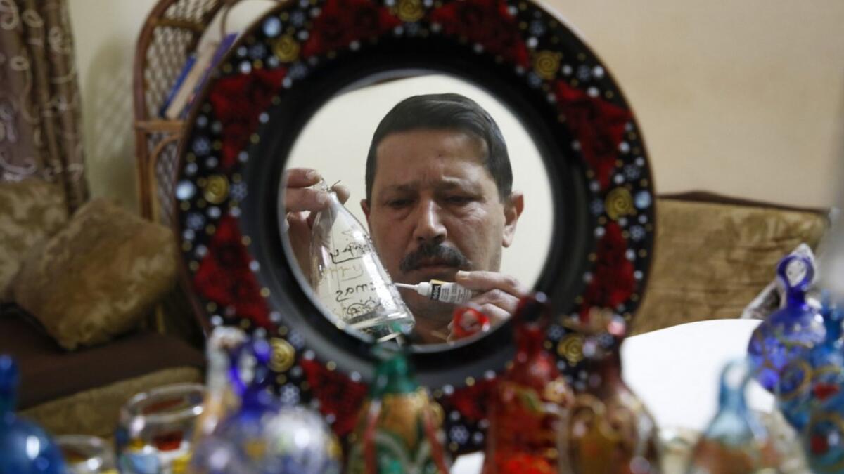 A Palestinian craftsman is reflected in a mirror as he decorates glass Christmas ornaments at a workshop in the southern West Bank city of Hebron, on December 15, 2019. HAZEM BADER / AFP