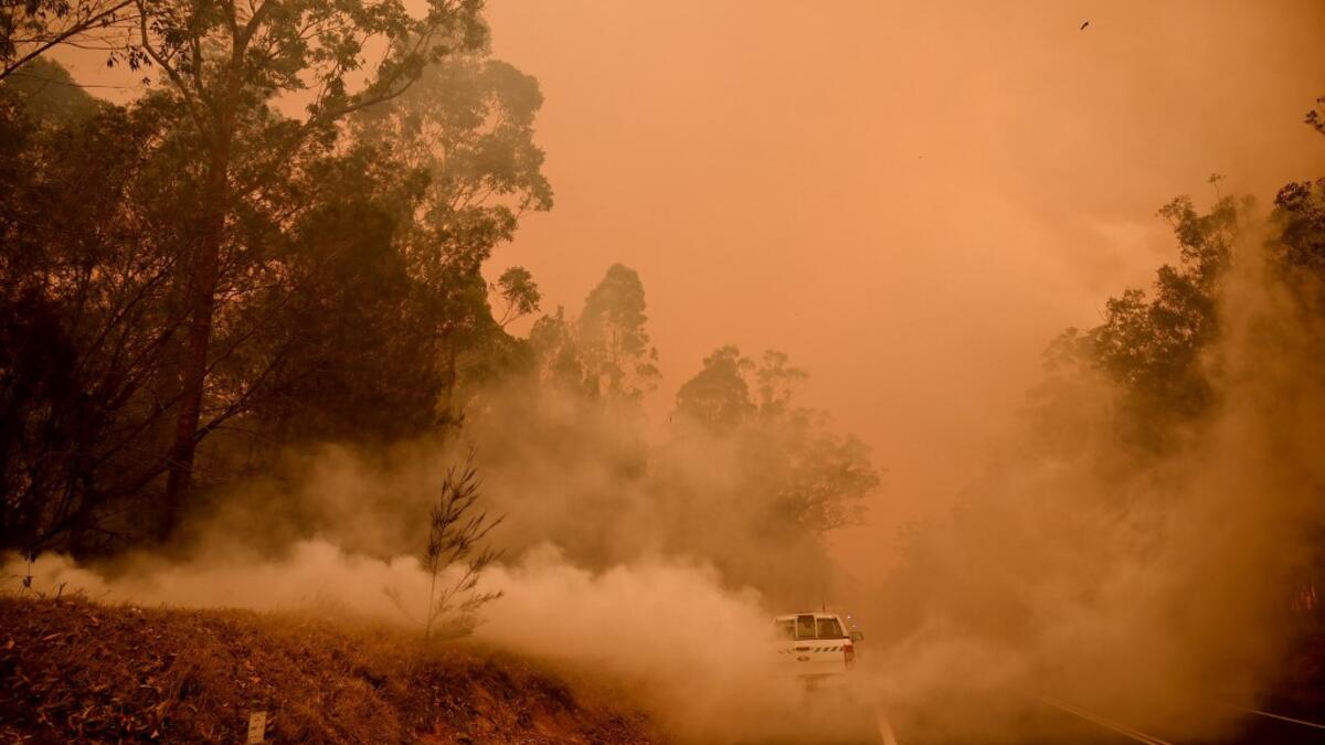 Firefighters tackle a bushfire in thick smoke in the town of Moruya, south of Batemans Bay, in New South Wales on January 4, 2020. Up to 3,000 military reservists were called up to tackle Australia's relentless bushfire crisis on January 4, as tens of thousands of residents fled their homes amid catastrophic conditions. PETER PARKS / AFP
