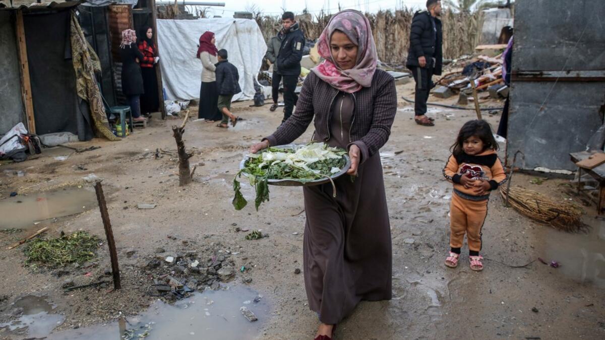 A Palestinian woman carries vegetables to her shack in Khan Yunis in the southern Gaza Strip on January 10, 2020. A family of 17, whose house was destroyed by an Israeli air strike last November, now live in a shack in cold weather and heavy rain. SAID KHATIB / AFP