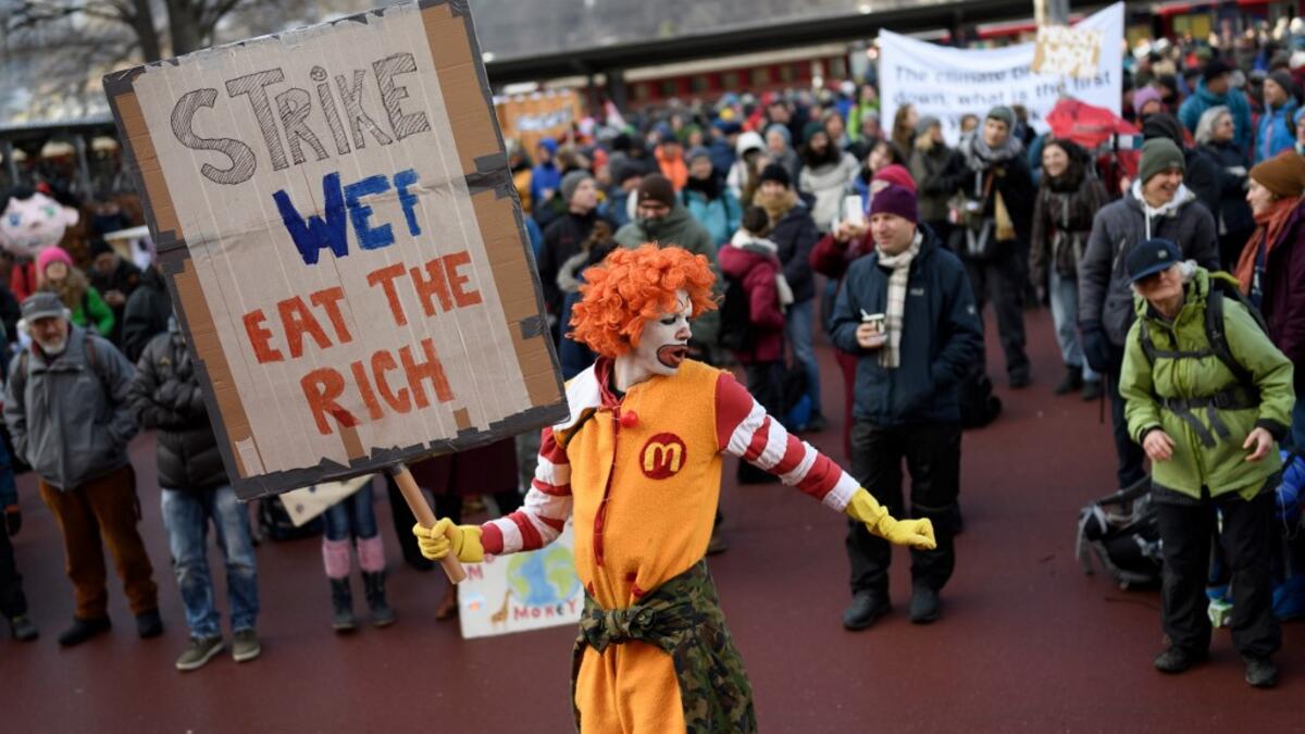 A man dressed as Ronald McDonald, the clown character used as the primary mascot of the McDonald's fast-food restaurant chain, holds a placard as he takes part in a gathering called by climate activists prior to the start of a march to Davos ahead of the World Economic Forum in January 19, 2020 in Landquart. FABRICE COFFRINI / AFP