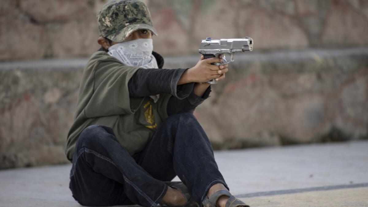 A boy aims a gun as the Regional Coordinator of Community Authorities (CRAC-PF) community police force teaches a group of children how to use weapons, at a basketball court in the village of Ayahualtempan, Guerrero State, Mexico, on January 24, 2020. The CRAC-PF vigilante group trains children as young as five so they can protect themselves from drug-related criminal groups operating in the area. Pedro PARDO / AFP
