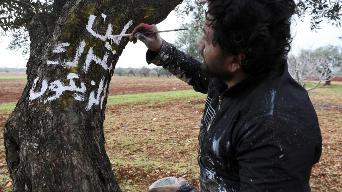 A Syrian man writes in white paint on the trunk of a tree the Arabic slogan "we will not abandon the olives", near the frontline between Syrian government forces and Turkish-backed opposition fighters in the town of Sarmin in the northern Syrian Idlib province on February 4, 2020. Omar HAJ KADOUR / AFP