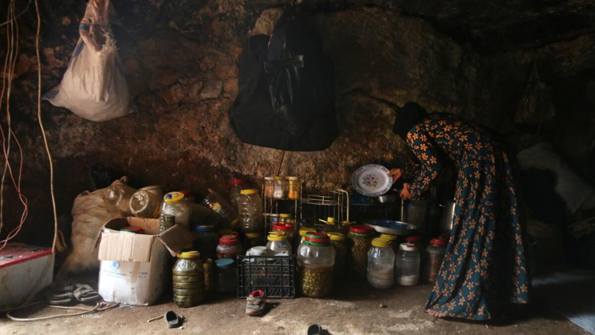 A woman holds a plate and a saucepan as she stands by food stores including pickled olives inside an underground shelter where several families of internally displaced Syrians from Aleppo and Idlib provinces are taking refuge, in the village of Taltunah about 15 kilometres northwest of Idlib in the northwestern Idlib province, on February 23, 2020. Aref TAMMAWI / AFP
