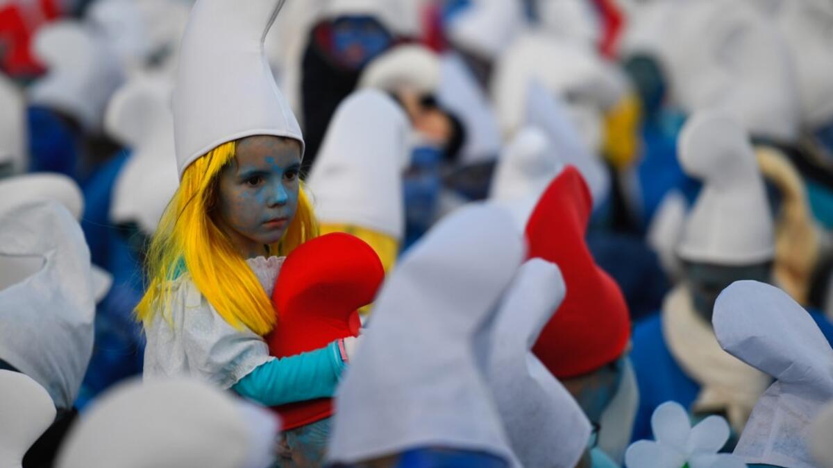 A child dressed as Smurfs ('Schtroumpfs' in French), a Belgian comic franchise centered on a fictional colony of small, blue, human-like creatures who live in mushroom-shaped houses in the forest, sits on the shoulders of an adult during a world record gathering of Smurfs on March 7, 2020, in Landerneau, western France. Damien MEYER / AFP