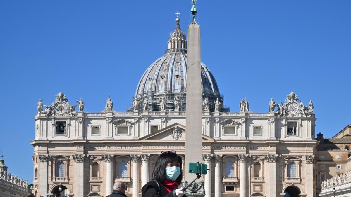 A photo taken on March 11, 2020 shows a tourist wearing a protective mask taking a selfie photo by the Vatican's Saint Peter's Square and its main basilica, a day after they were closed to tourists as part of a broader clampdown aimed at curbing the coronavirus outbreak. ANDREAS SOLARO / AFP