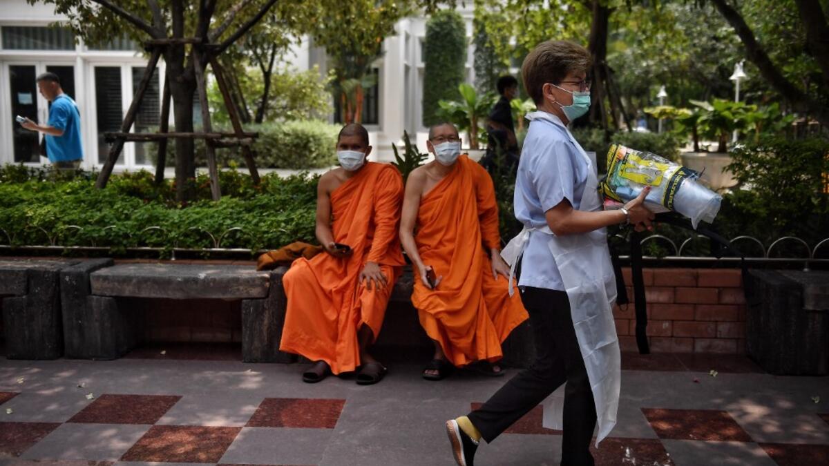 Monks wearing face masks sit outside a temple while a worker carries materials for use to disinfect the Wat Pak Nam Buddhist temple, as part of measures against the COVID-19 novel coronavirus, in Bangkok on March 16, 2020. Lillian SUWANRUMPHA / AFP