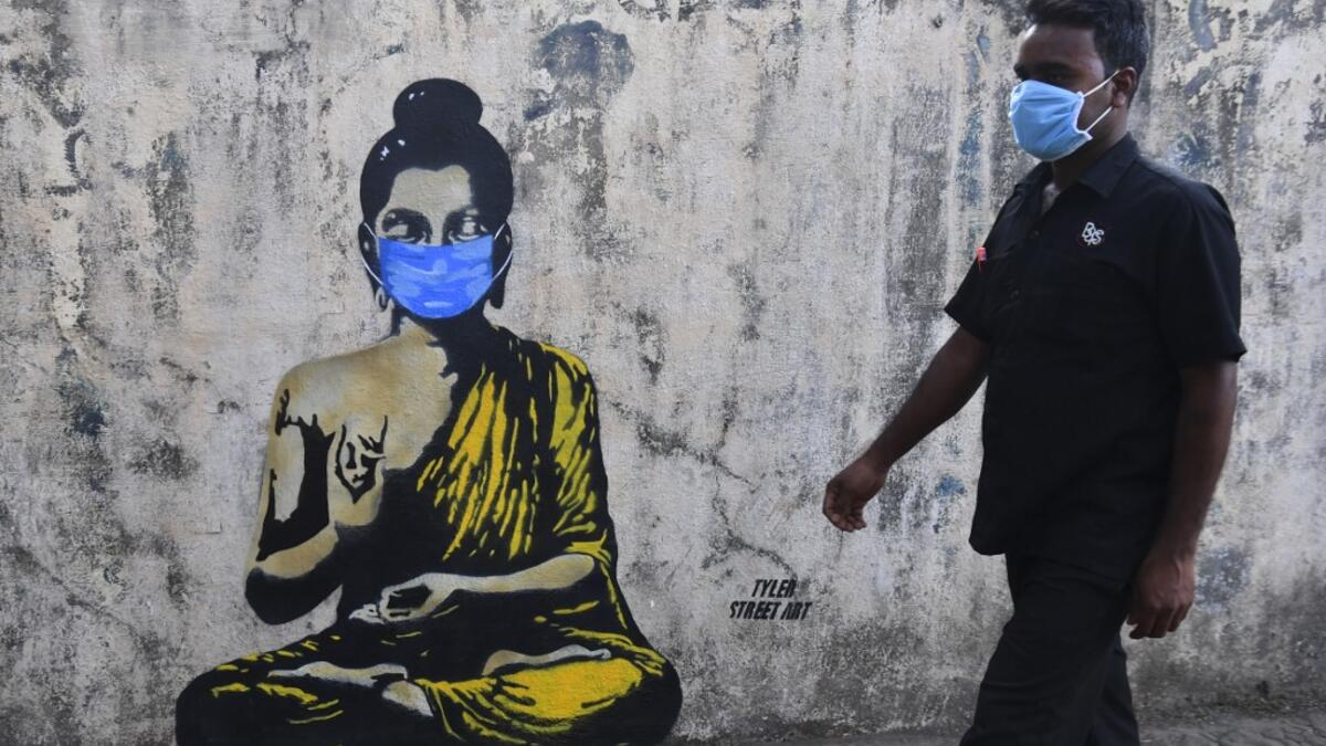 A resident wearing a facemask amid concerns over the spread of the COVID-19 novel coronavirus walks past a graffiti of Buddha wearing facemask, in Mumbai on March 16, 2020. INDRANIL MUKHERJEE / AFP