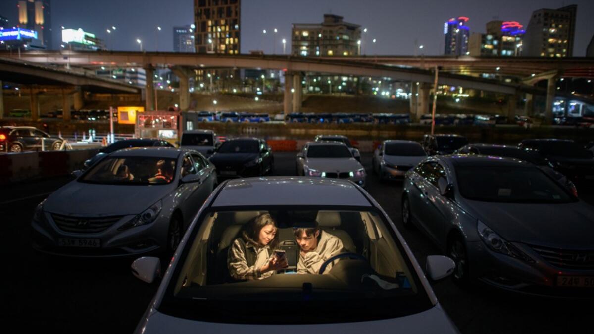 In a photo taken on March 21, 2020 a couple look at a mobile phone as they sit in a car at a screening at a drive-through cinema in Seoul. Box office numbers in South Korea -- which has 8,897 confirmed virus cases -- have plummeted in recent weeks due to the epidemic, with authorities urging the public to avoid large crowds. But at drive-in cinemas, moviegoers can enjoy a movie from the comfort of their cars, parked in front of a large outdoor screen.  Ed JONES / AFP