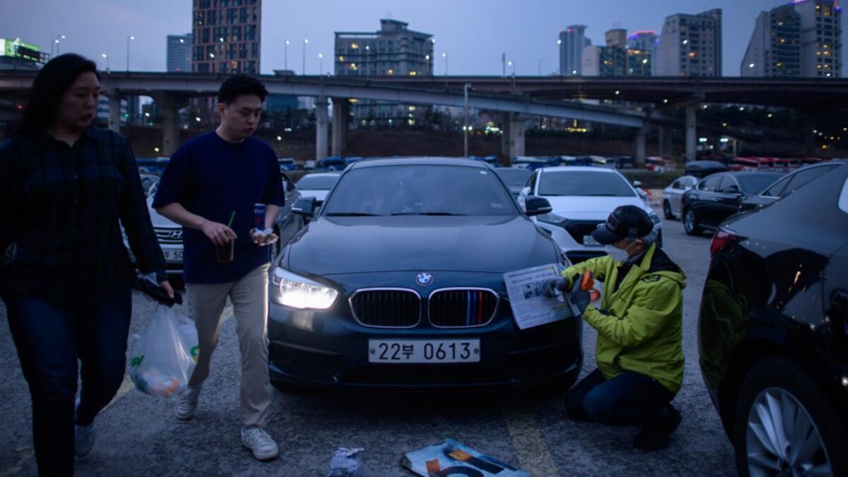 In a photo taken on March 21, 2020 a staff member secures newspaper over the headlights of cars prior to a screening at a drive-through cinema in Seoul. Box office numbers in South Korea -- which has 8,897 confirmed virus cases -- have plummeted in recent weeks due to the epidemic, with authorities urging the public to avoid large crowds. But at drive-in cinemas, moviegoers can enjoy a movie from the comfort of their cars, parked in front of a large outdoor screen.  Ed JONES / AFP