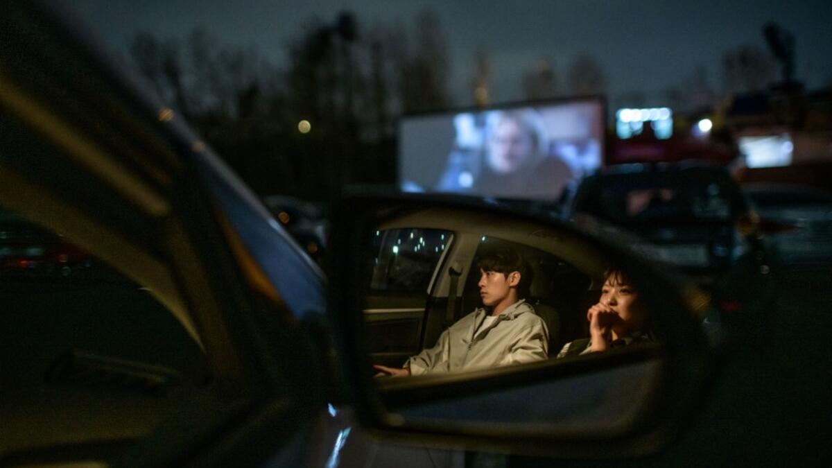 In a photo taken on March 21, 2020 a couple sit in their car as they watch a movie screening at a drive-through cinema in Seoul. Box office numbers in South Korea -- which has 8,897 confirmed virus cases -- have plummeted in recent weeks due to the epidemic, with authorities urging the public to avoid large crowds. But at drive-in cinemas, moviegoers can enjoy a movie from the comfort of their cars, parked in front of a large outdoor screen.  Ed JONES / AFP