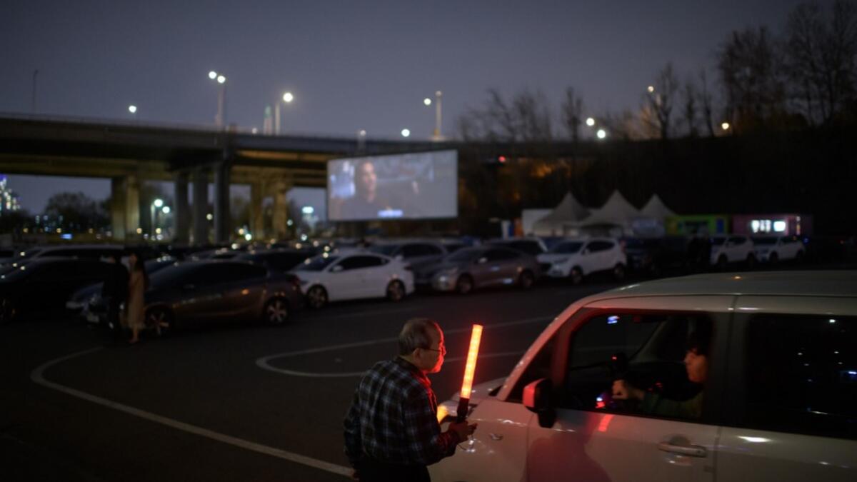 In a photo taken on March 21, 2020 an usher directs customers and their cars to a movie screen at a drive-through cinema in Seoul. Box office numbers in South Korea -- which has 8,897 confirmed virus cases -- have plummeted in recent weeks due to the epidemic, with authorities urging the public to avoid large crowds. But at drive-in cinemas, moviegoers can enjoy a movie from the comfort of their cars, parked in front of a large outdoor screen.  Ed JONES / AFP