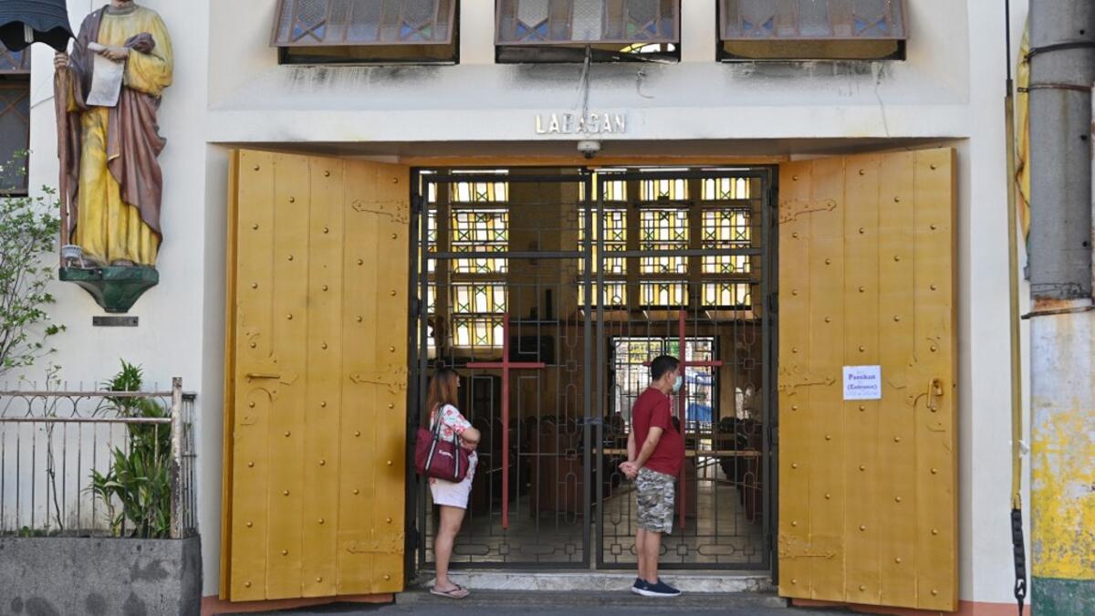 People wearing face masks stand and pray outside an empty Quiapo church, usually filled with devotees during Fridays but now closed due to restrictions to stop the spread of the COVID-19 coronavirus, in Manila on March 27, 2020. Catholic church authorities closed all its churches in line with the government's imposed enhanced quarantine as a preventive measure against COVID-19. Ted ALJIBE / AFP