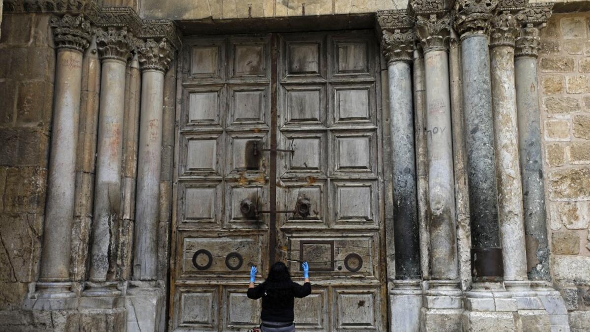 A woman prays in front of the Church of the Holy Sepulchre in the Old City of Jerusalem following the closure of the city for non-residents as a measure to contain the spread of the novel coronavirus, on March 30, 2020. MENAHEM KAHANA / AFP