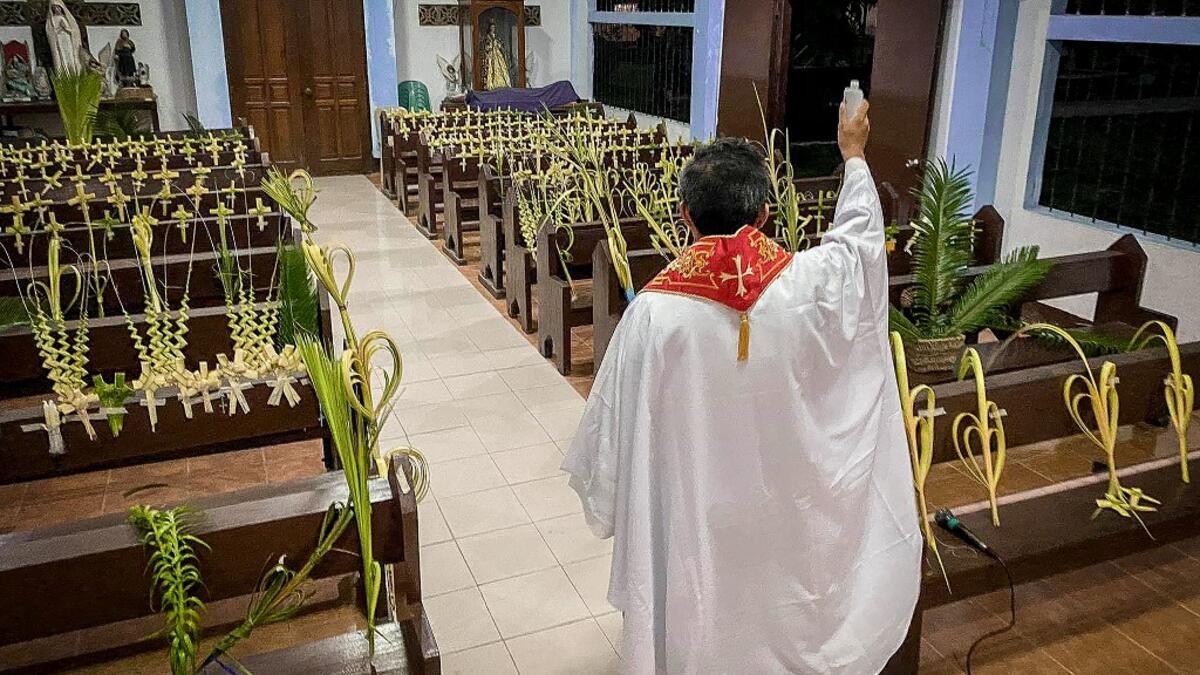 A Roman Catholic priest blesses palm branches occupying church pews during Palm Sunday event in Borongan town, Eastern Samar province, central Philippines on April 5, 2020. Alren BERONIO / AFP