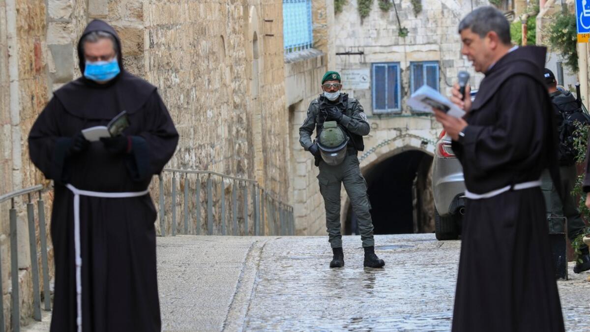 An Israeli soldier stands guard as Fransiscan friars pray at the first station while taking part in a small Procession of the Way of the Cross along the Via Dolorosa to mark Good Friday in Jerusalem, on April 10, 2020, amid the COVID-19 outbreak. All cultural sites in the Holy Land are shuttered, regardless of their religious affiliation, as authorities seek to forestall the spread of the deadly respiratory disease, which will prevent Christians from congregating for the Easter service, this coming Sunday f