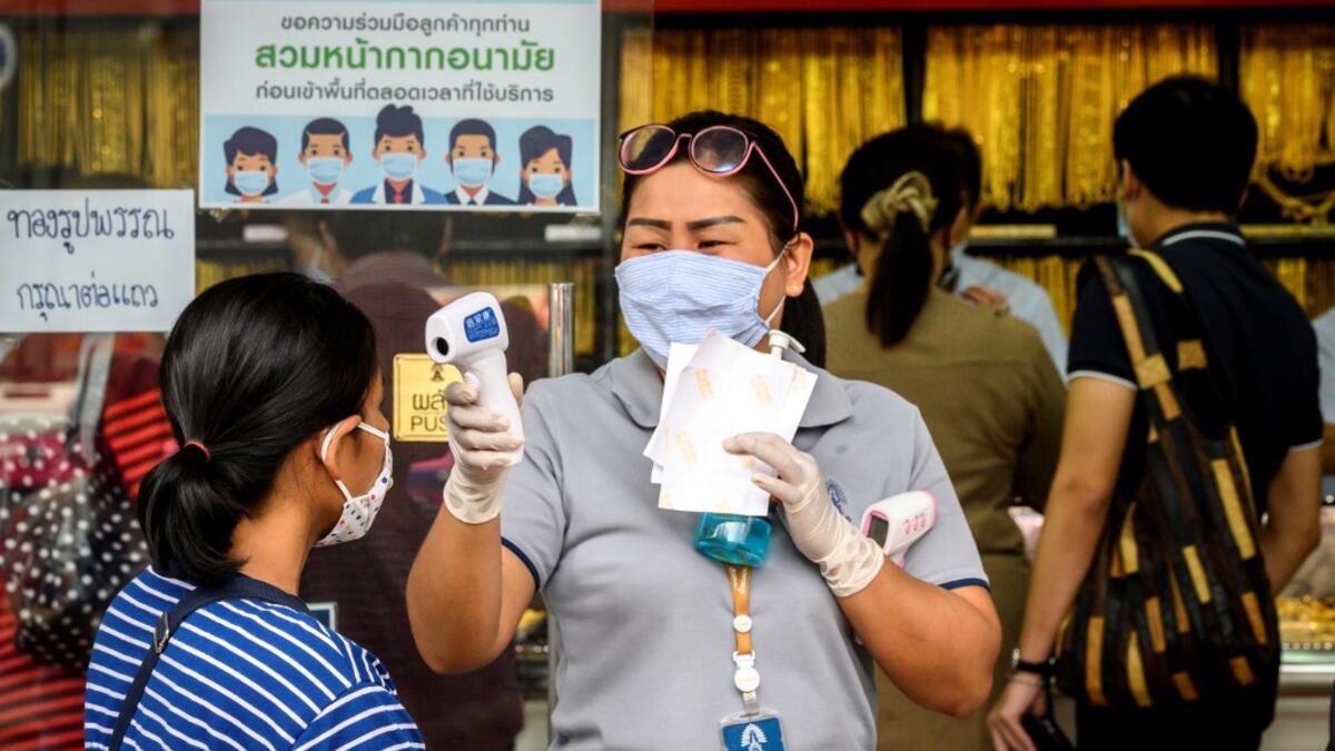 An employee wearing a face mask amid fears of the spread of COVID-19 coronavirus checks the temperature of a customer outside a gold shop in Bangkok's Chinatown on April 15, 2020. Hundreds of Bangkok residents rushed to goldsmith shops in order to sell their jewelries as gold prices reached its highest levels since 2012. Mladen ANTONOV / AFP