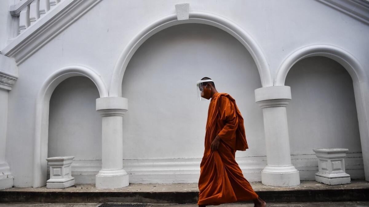 A novice monk wearing a face shield as a preventive measure against the spread of the COVID-19 coronavirus walks through Wat Molilokkayaram Buddhist temple in Bangkok on April 20, 2020. Lillian SUWANRUMPHA / AFP
