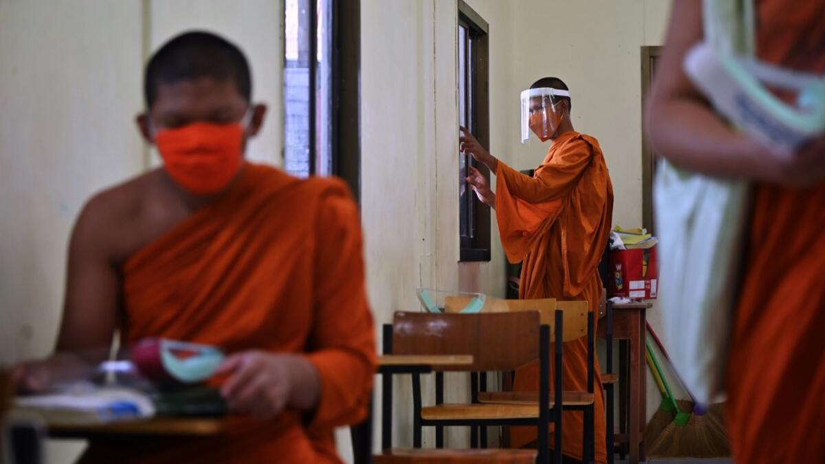 A novice monk wearing a face shield as a preventive measure against the spread of the COVID-19 coronavirus closes the window of a classroom before religious studies at Wat Molilokkayaram Buddhist temple in Bangkok on April 20, 2020. Lillian SUWANRUMPHA / AFP