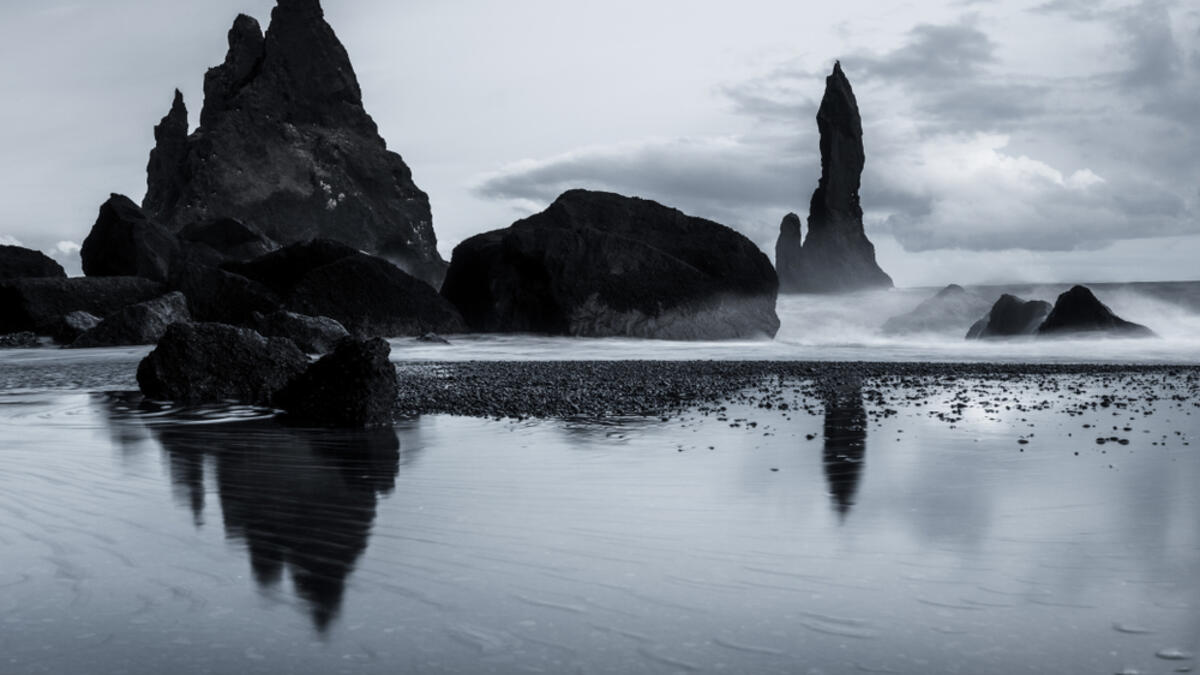 Rock formations on a black sand beach in Iceland with reflection in the Sea and a dark sky in misty moody weather with dark colors and a rough sea (Shutterstock)